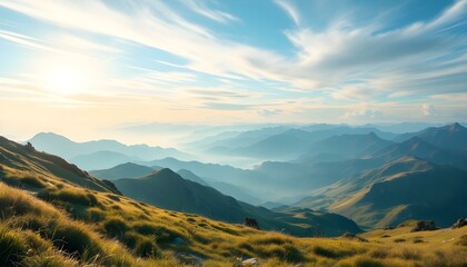 Fototapeta premium Panoramic view of a sunrise over misty mountains, with golden light illuminating grassy hills, peaks, and layers of distant mountains under a vibrant blue sky streaked with soft clouds.