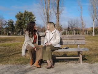 Blind woman sits on a park bench, smiling while talking with her friend. Her white cane rests...