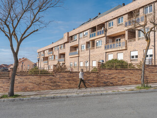 Blind young woman walking uphill on a city sidewalk using a white cane for guidance. Concept of...
