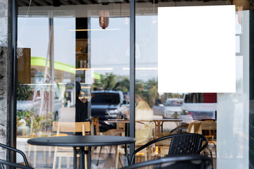 A white sign hangs from the window of a restaurant. Poster promotion design mockup.
