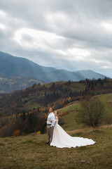 couple standing against the backdrop of a picturesque mountain landscape. A man and a woman look at each other.