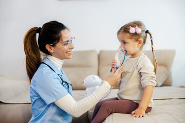 A little girl is inhaling medicine through nebulizer and her pediatrician in helping her during her...
