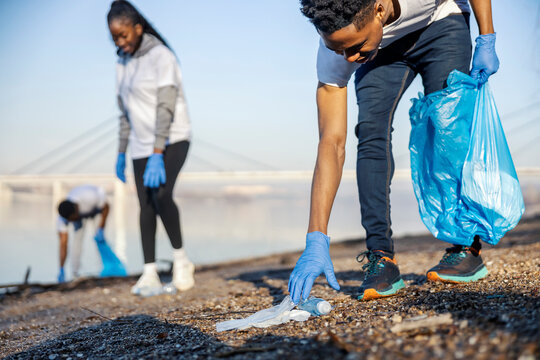 Group of three diverse eco activists collecting plastic waste at riverbank in nature. Save the planet.