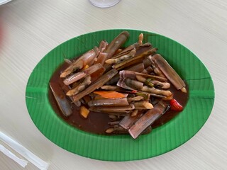 A Chinese Dish Bamboo clams steamed in sweet and sour sauce garnished with Spring Onions and Fried Garlic on green plate