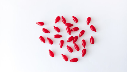 A number of oval-shaped red capsules are scattered on a white table