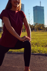 Young woman stretching after exercising and jogging in urban park during sunny summertime day.