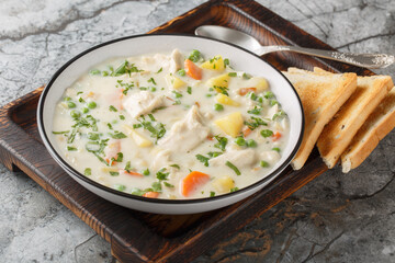 Comfort chicken pot pie soup with potatoes, carrots and green peas in a spicy creamy broth close-up in a bowl on the table. Horizontal