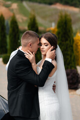 A man in a black suit and white shirt hugs a woman who is wearing a white dress with shiny elements.