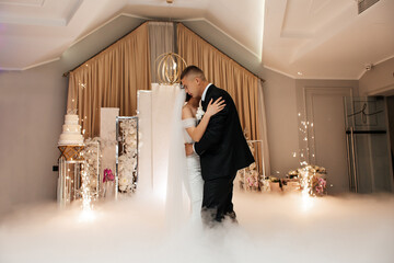 The bride and groom dance surrounded by thick white smoke, creating the effect of clouds.