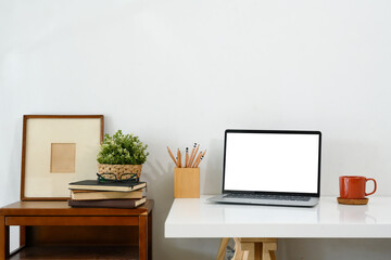 Creative workspace with blank screen laptop, coffee mug and picture frame