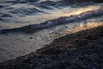 Water reaching the shore of a pebble beach in the afternoon sun. With space to copy. High quality photo