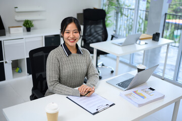 Fototapeta premium Cheerful businesswoman sitting at her desk in a modern office, smiling at the camera