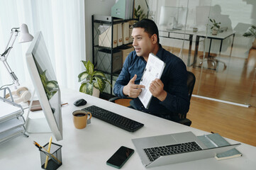 Naklejka premium Man in office holding tablet while speaking during a video call, engaging with colleagues through virtual meeting on computer screen, showcasing presentation