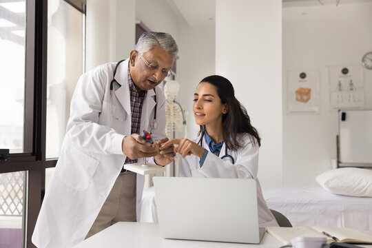Doctor teamwork. Two diverse colleagues cardiologists elderly male young female in white coats engaged in medical research study heart anatomy using model notebook collaborate discuss clinical case