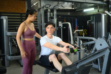 Fototapeta premium Female coach supervising a male client working out on rowing machine in a modern gym