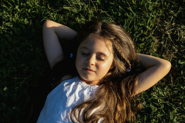 A girl in a white dress lies on the green grass in a park on a summer day. view from above
