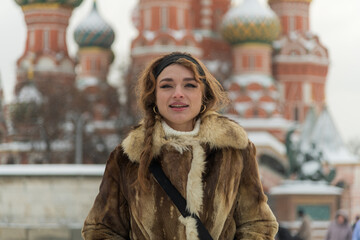 Woman in a fur coat enjoying winter near St. Basil's Cathedral in Moscow with colorful domes in the...