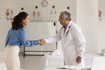 Obraz premium Partnership in healthcare. Happy mature man doctor medic worker young woman patient pharmaceutical company representative shake hands on meeting at clinic glad satisfied with successful collaboration