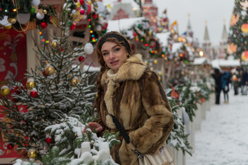 Woman in fur coat enjoying winter festivities at a decorated market during a snowy day