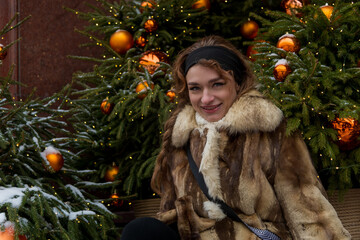 Young woman in fur coat poses beside festive holiday decorations in snowy winter scene