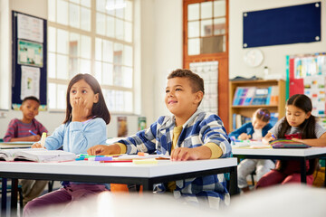 Group of happy elementary classmates listening to teacher during lesson