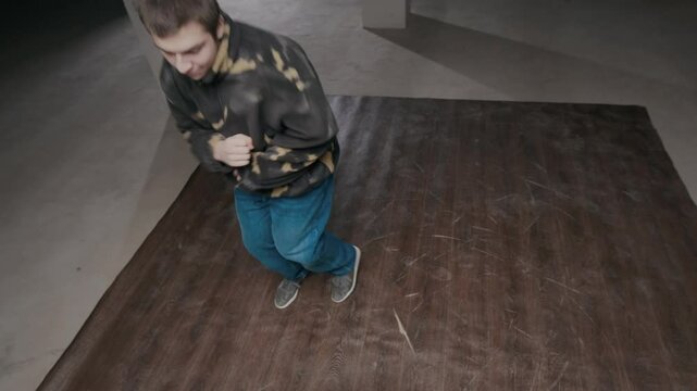 Handheld high angle shot of confident Caucasian gen Z b-boy in urbanwear improvising top tock movements while breaking in dance hall
