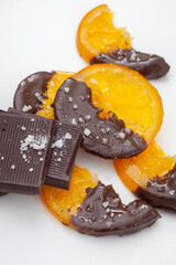 A plate of chocolate covered oranges and a chocolate bar with salt on a white background