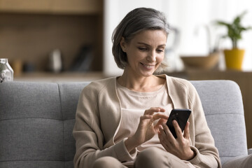 Digital entertainment. Modern day smiling mature woman confident phone user enjoy weekend at home...