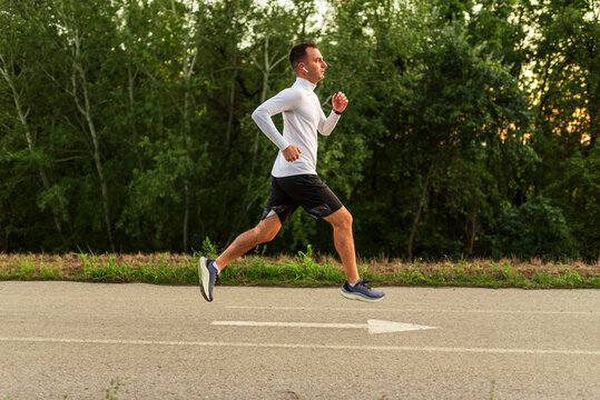 Young sportsman running in park wearing wireless earphones