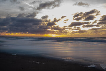 A beautifully peaceful sunset occurs as gentle waves tenderly caress the sandy shore, evoking deep...