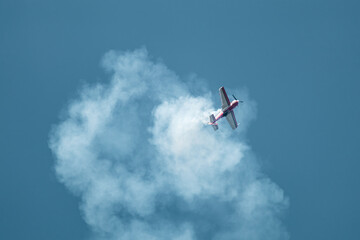 Light red Su-31 airplane with vapor contrails in blue sky on airshow