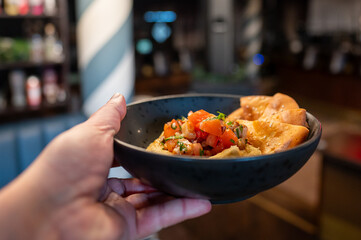 A freshly plated dish featuring thinly sliced meat with a garnish of greens, served in a stylish black bowl. The background showcases a vibrant restaurant setting with colorful decor.