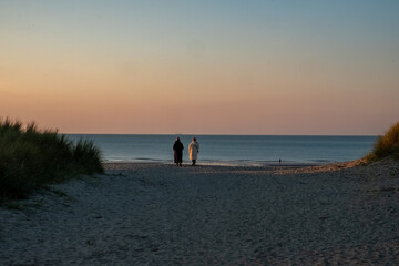 A tranquil beach scene at dusk with a loving couple leisurely walking hand in hand along the serene...