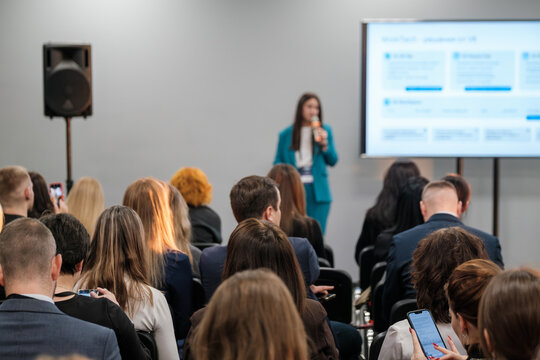 Audience listens to speaker at business conference. Presentation focuses on modern strategies, trends. Engaged participants take notes.