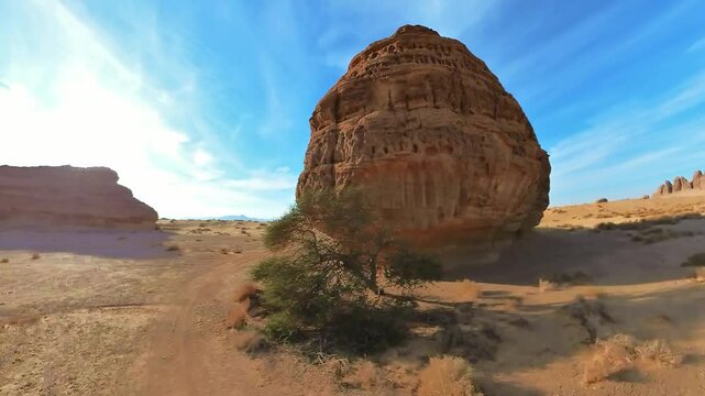 hyperlapse around the Qasr Al Farid, the tomb of Lihyan son of Kuza, rises majestically in the Hegra desert of Al-Ula, Saudi Arabia. displaying intricate Nabataean rock cut architecture under blue sky
