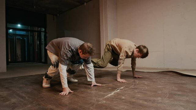 Handheld shot of two talented Caucasian male zoomers in streetwear performing creative choreographed breakdance full of energy and style, practicing together indoors