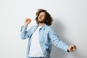 Happy young man dancing joyfully against a light background, wearing a casual denim jacket and a...