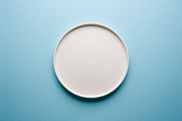 Top view of empty ceramic white plate on blue background