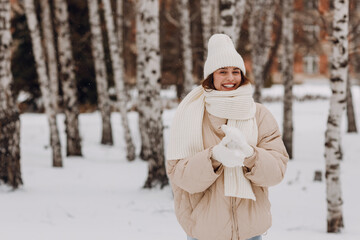 Happy smiling young woman portrait dressed coat scarf hat and mittens enjoys winter weather at birch winter park