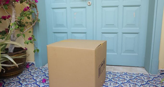 Male courier placing cardboard box at customers door, leaving entrance. Female client, recipient of parcel opening door, taking package, getting purchase via contactless delivery service