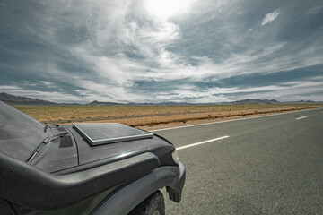 An off-road car with a solar panel stands on the highway with a view of the blue sky and the steppe. An electric car with a solar battery stands against the background of a steppe and a road.