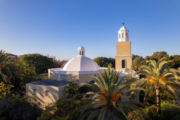 Aerial view of dome and tower of Virgen del Rocio parish in San Pedro de Alcantara, Marbella, Spain. Exterior architecture of roof surrounded by palm trees against a clear blue sky