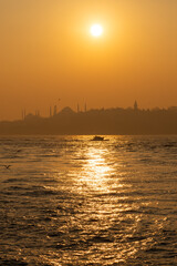 High resolution panoramic photograph capturing Istanbul's historic peninsula bathed in a crimson sunset glow. The city's iconic skyline silhouettes against the vibrant evening sky