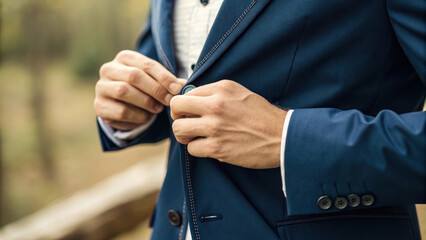 Buttoning up stylish blue jacket in natural outdoor setting, showcasing elegance and attention to detail