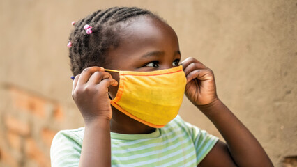 child wearing yellow face mask, adjusting it with care, showcasing resilience and safety
