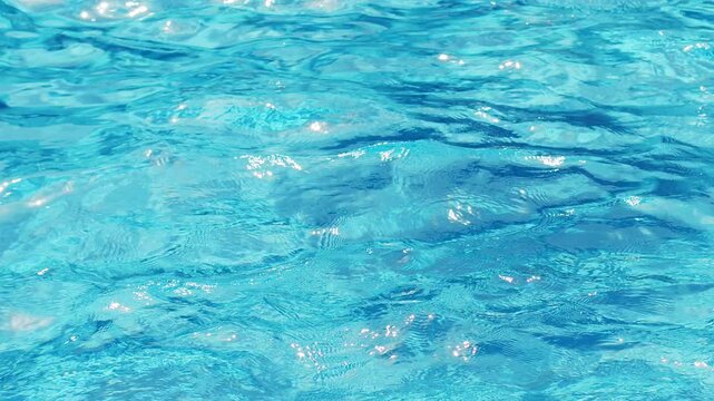 Ripples on the water of the pool, transparent, sparkling, inviting surface of the water in motion, view from above. Slow motion and looped video.
