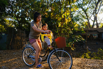 Obraz premium Little boy sitting on bike chair with mom ride bicycle sunset light outdoor park