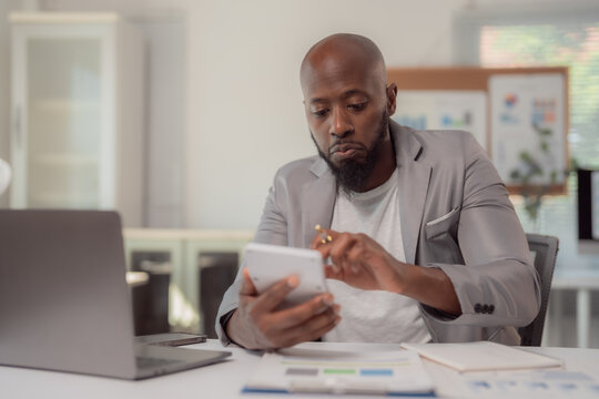 Focused african american businessman is using a calculator and reviewing financial documents, performing calculations for budget analysis and financial planning in his modern office