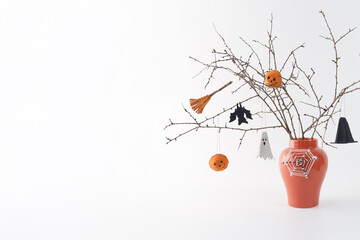 Dry branches with Halloween ornaments in orange vase. Minimal holiday decoration ghost, witch hat, broom, spiderweb.  still life on white background. Halloween celebration and home decor concept,