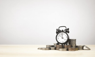 Black alarm clock on pile fo coins with copy space. Concepts of time management, financial...